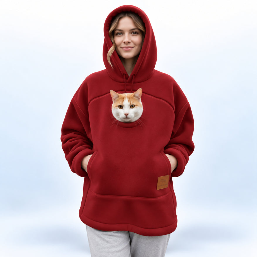 A woman wearing a red hoodie with a realistic cat face printed on the chest, standing against a soft light blue gradient background.